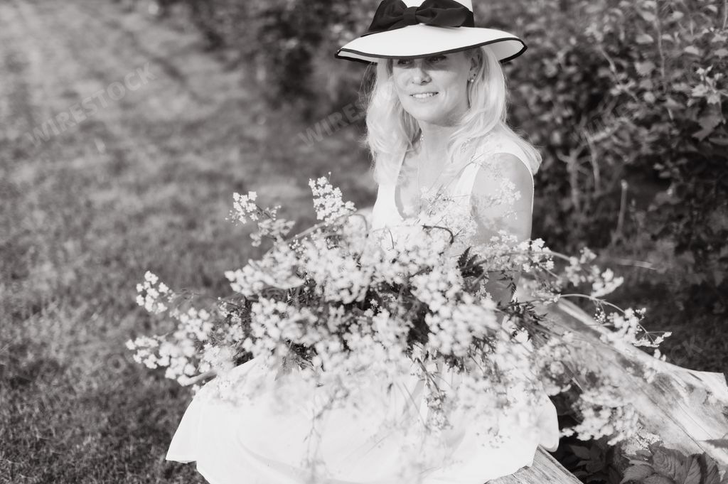 A grayscale of a beautiful blonde woman holding a bouquet of flowers in a field