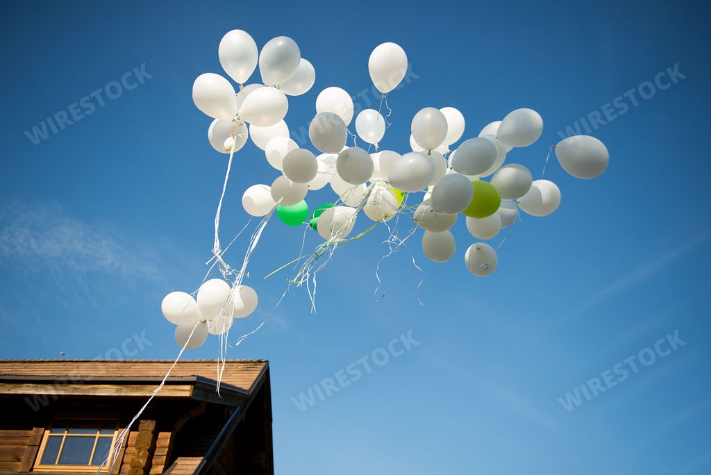 A low angle shot of a bunch of white wedding balloons floating in a blue sky