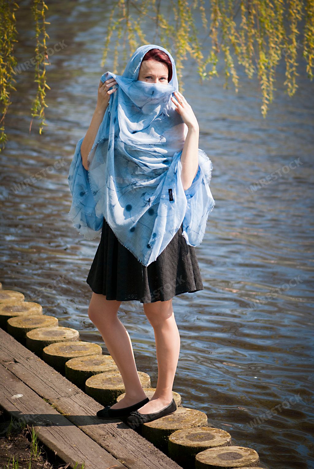 A vertical shot of a beautiful Caucasian woman posing with her scarf near a lake during summer