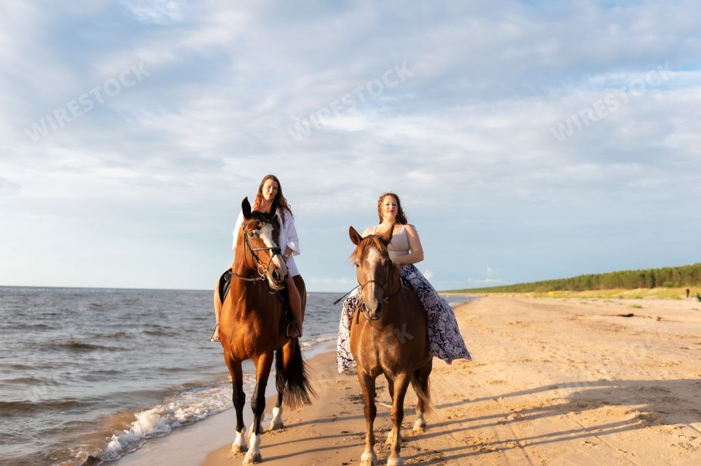 The two young female friends riding horses together on a sunny beach