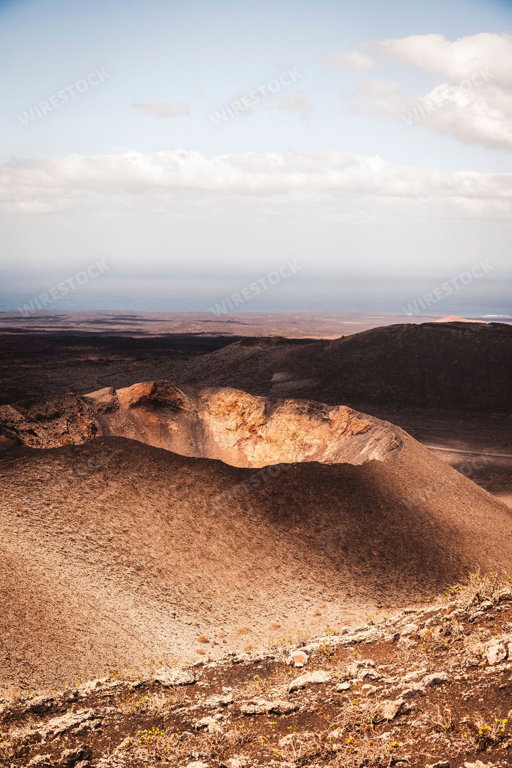 A vertical shot of a desert with a cloudy blue sky in the background Timanfaya National Park, Spain