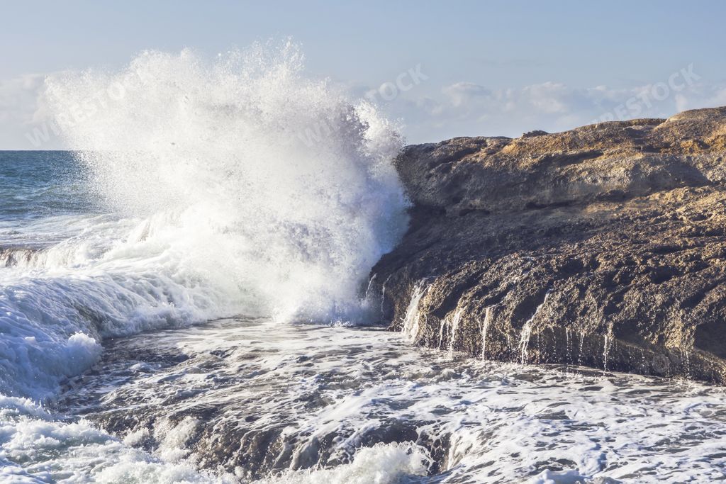 A beautiful scenery of sea waves splashing near a rock formation during daytime