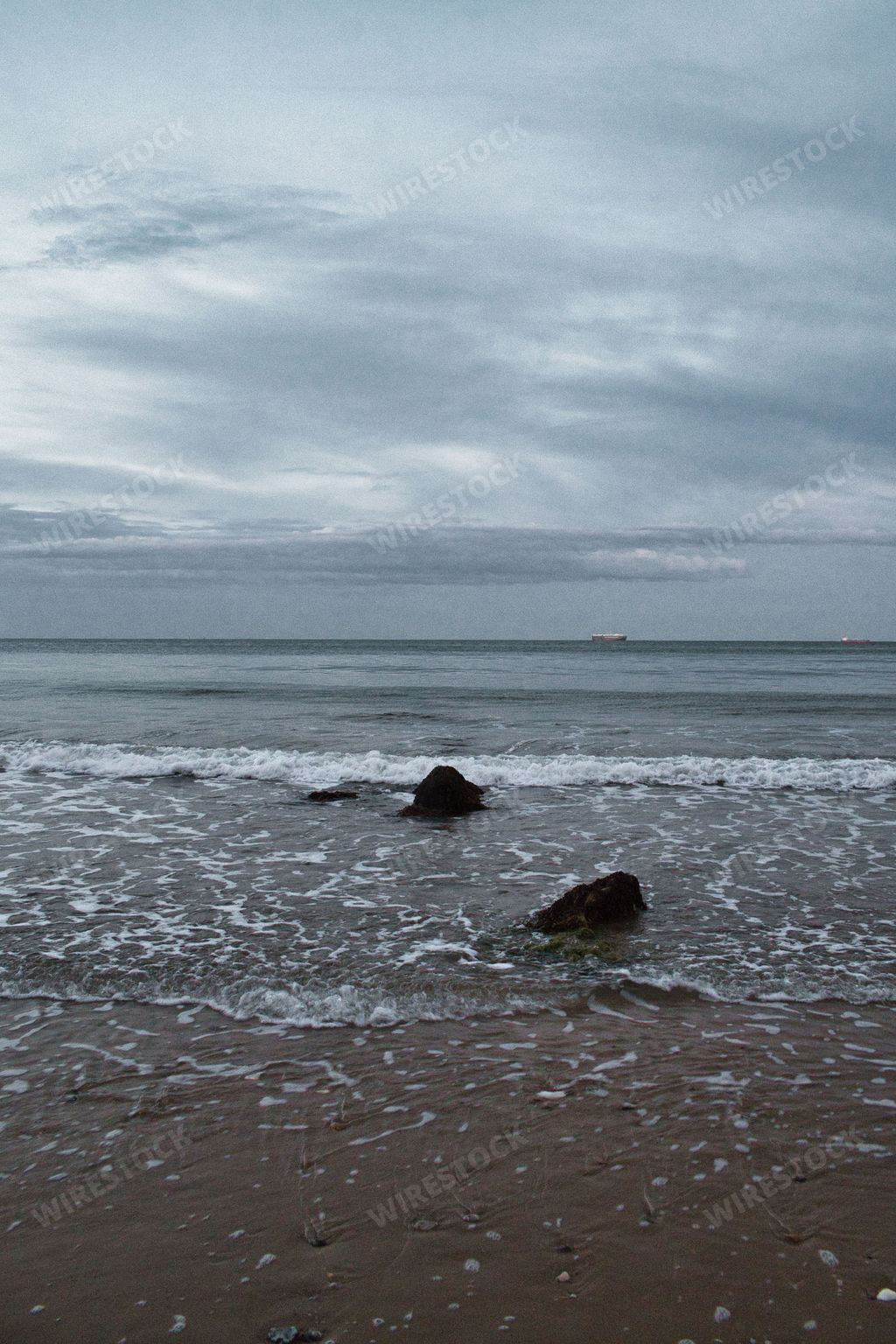 A vertical view of the sandy shore before the seascape under the cloudy sky