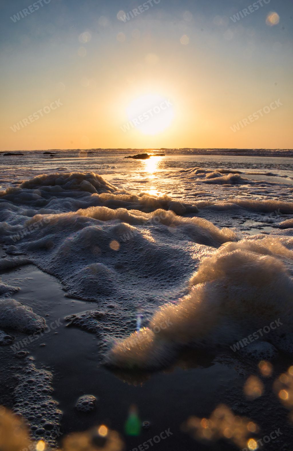 A vertical shot of the sun setting and reflecting on the surface of the ocean