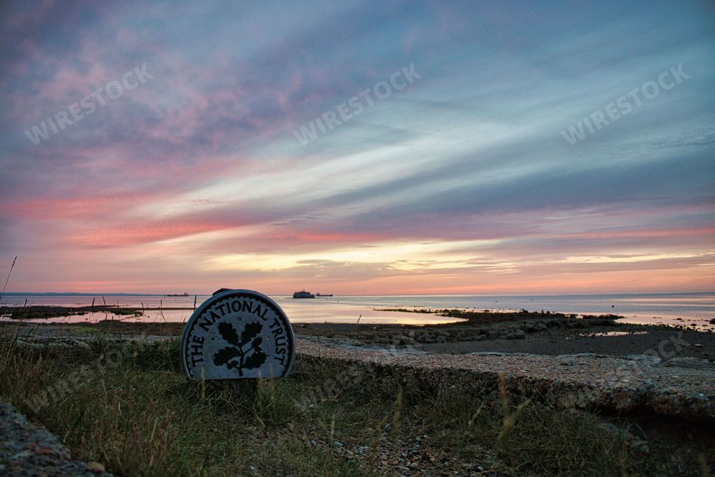 A blue and pink sky over a rocky and grassy beach with sign "The National Trust"  in Isle of Wight