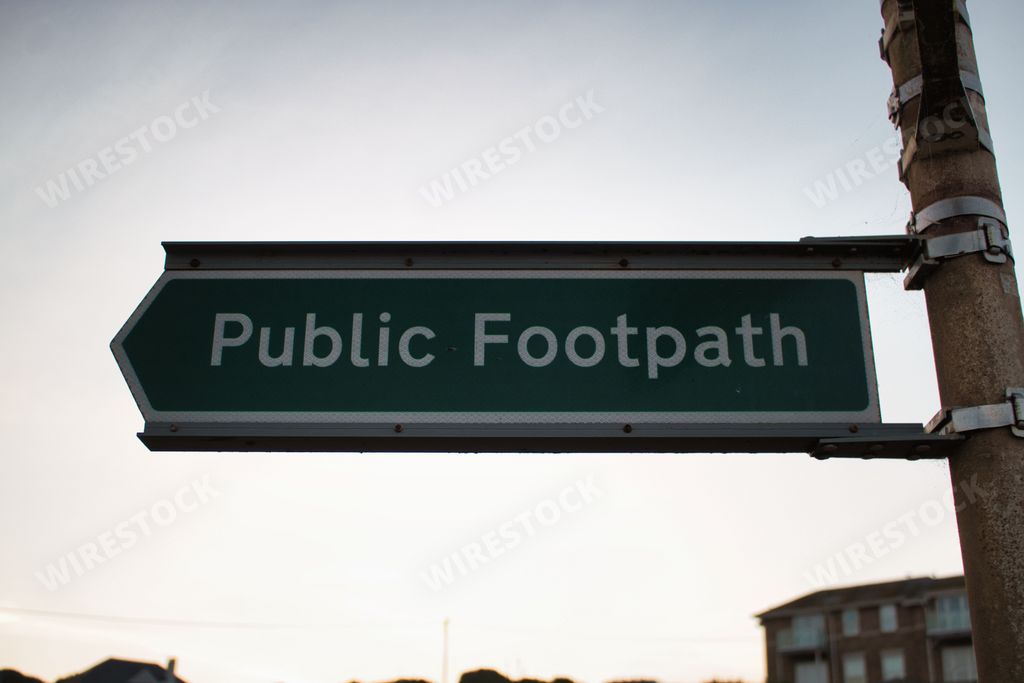 A closeup shot of a sign reading "Public Footpath" fixed on a pole against the sky
