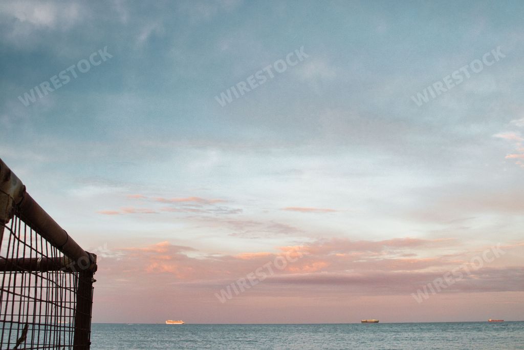 The view from the side of a fence to the seascape and boats under the cloudy sky