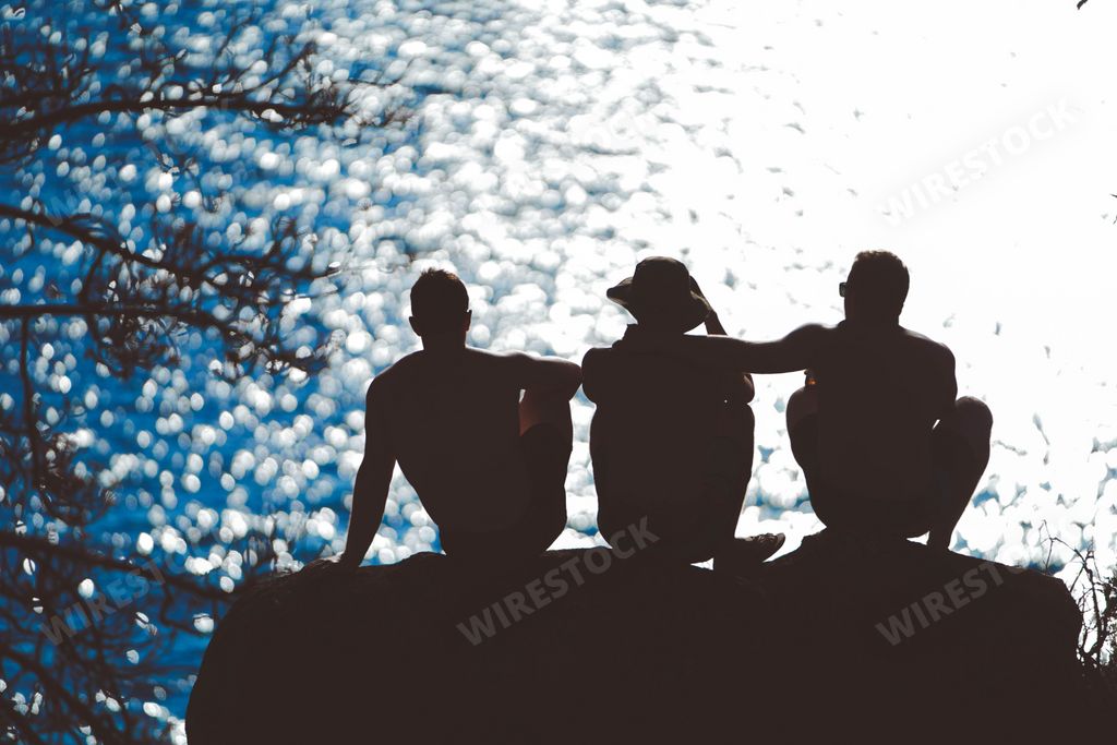 A silhouette of three friends sitting on a rock near the sea enjoying each others company in the evening