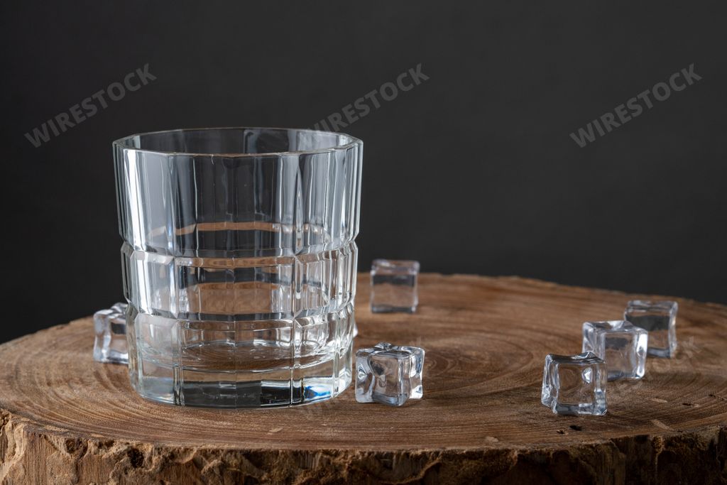 A closeup shot of an empty clear glass with ice cubes on a wooden surface