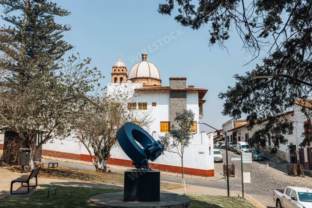 A picturesque view of a colonial town with a church dome and modern sculpture in the park