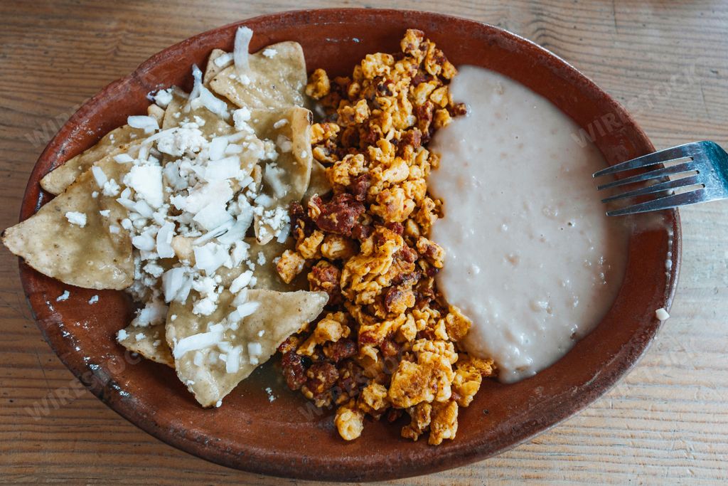 A traditional Mexican breakfast plate with chilaquiles, scrambled eggs with chorizo, and refried beans on a wooden table