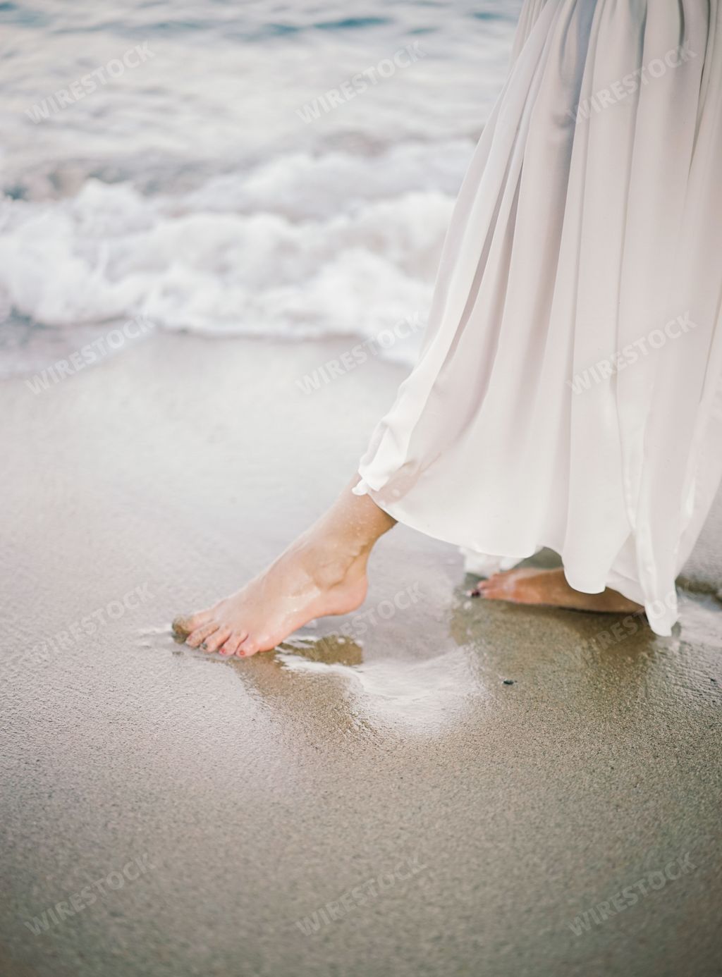 A close-up of a person walking barefoot on the beach with waves gently touching the sand