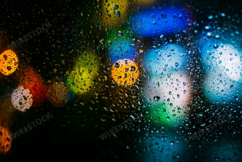 A macro shot of raindrops on a car window with colorful bokeh lights in the background