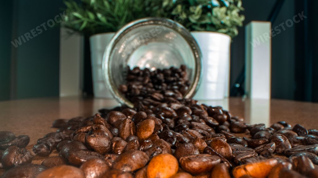 A closeup shot of coffee beans pouring from glass transparent jar on a background of home plants