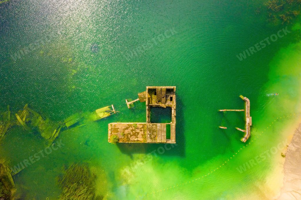 An aerial view of the Rummu abandoned prison, partially submerged in a lake surrounded by forest trees in Tallinn, Estonia