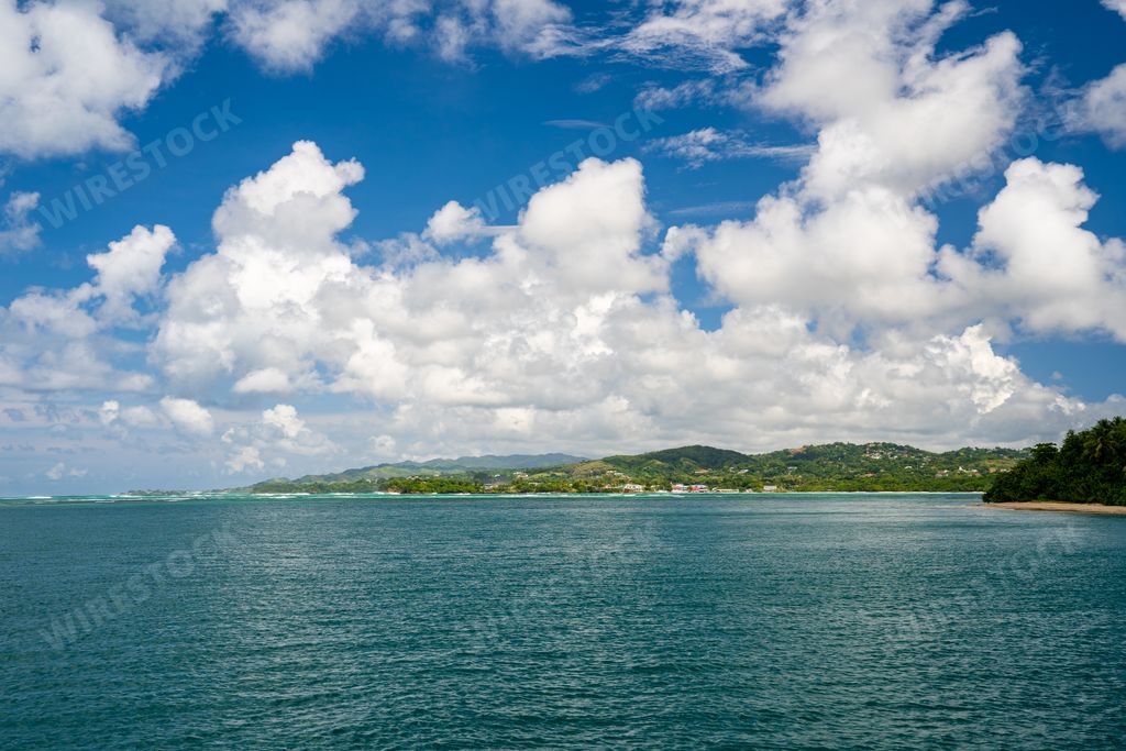 A landscape of the sea surrounded by hills covered in greenery under a blue cloudy sky