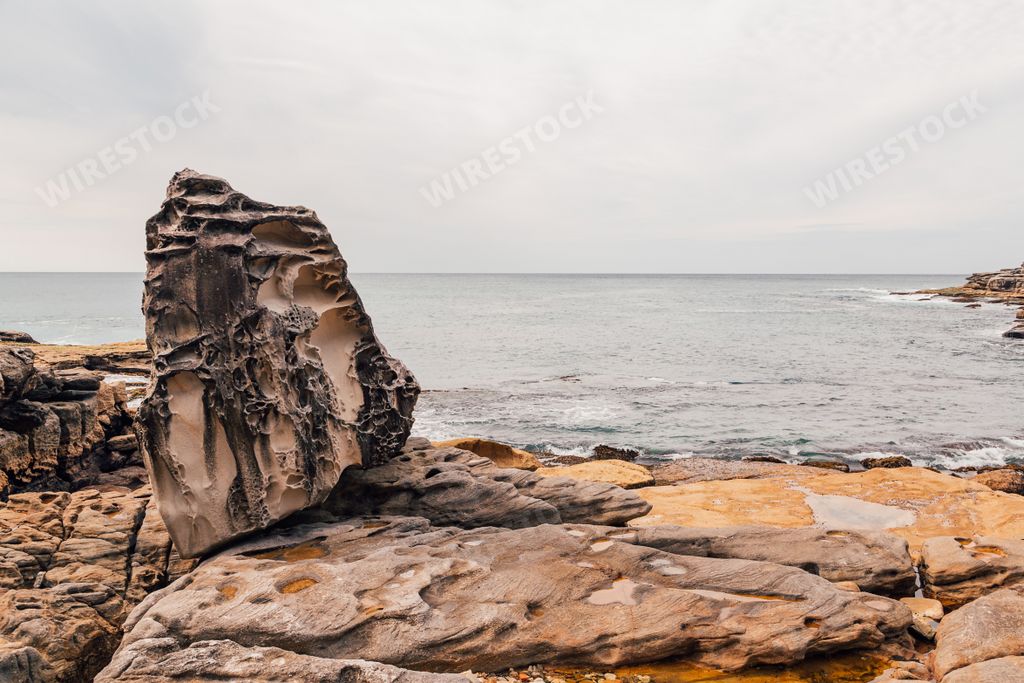 The shoreline covered in rocks surrounded by the sea under a cloudy sky