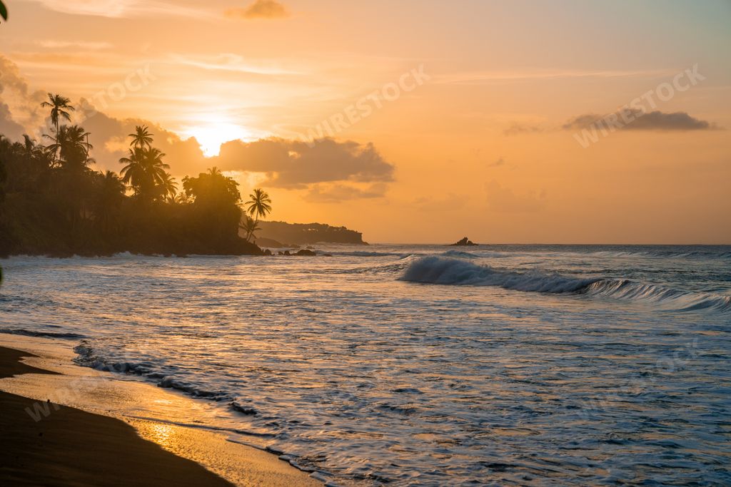 The ocean waves hitting the sandy beach and gleaming under the sunset