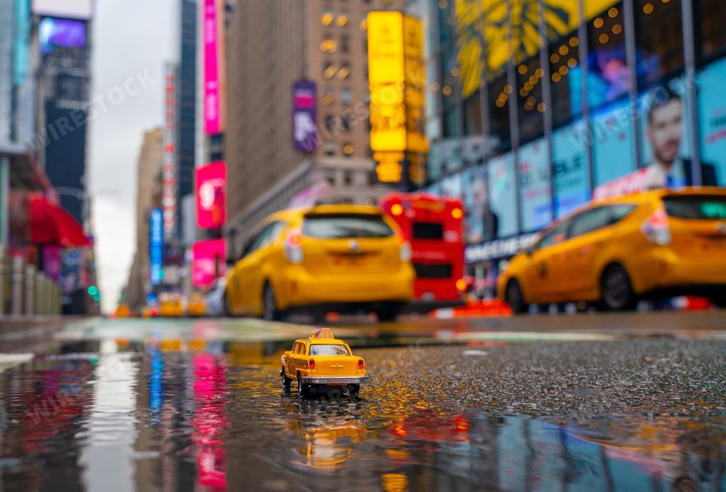 A closeup shot of a toy yellow taxi cab on a road with real taxis on the background