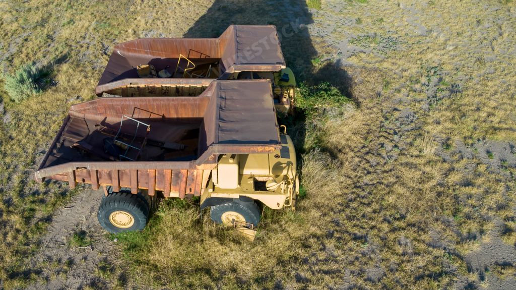 An aerial shot of two abandoned large mining trucks in an open field