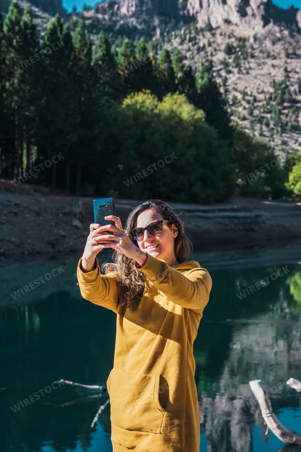 A vertical shot of a caucasian woman taking a selfie in front of a lake