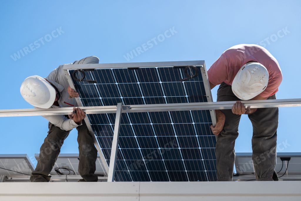 The two men installing a solar panel on the rooftop.