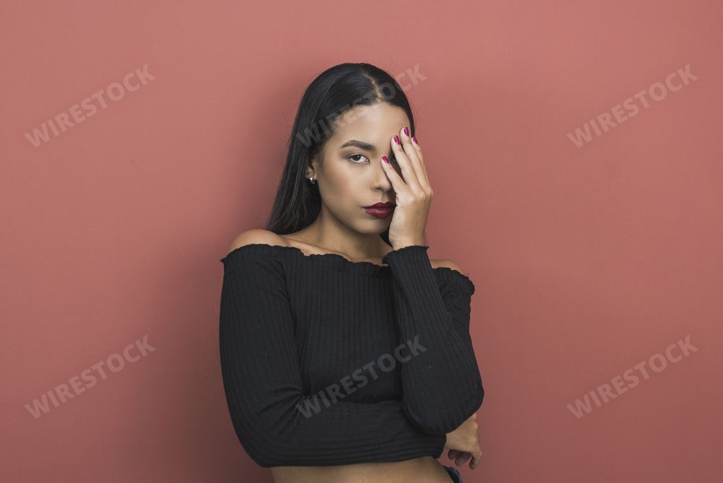 A beautiful shot of a sexy Hispanic woman with red lipstick and open shoulders posing on a pink background