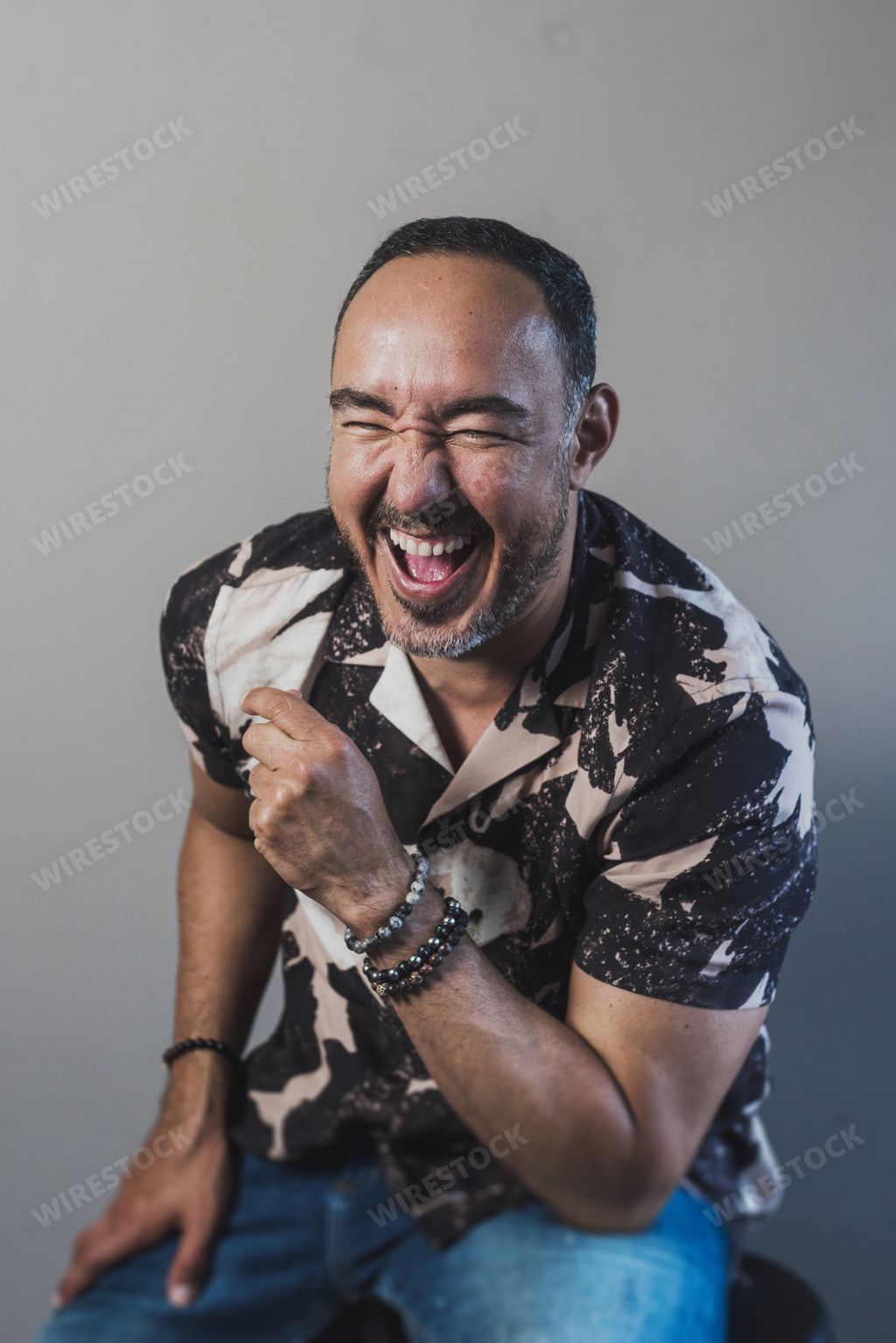 A vertical shot of a happy laughing adult male sitting on a chair on a grey background