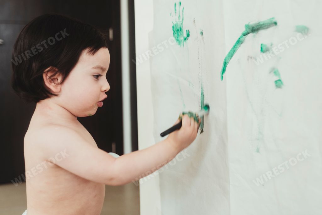 A closeup shot of a toddler drawing on the wall with a paintbrush