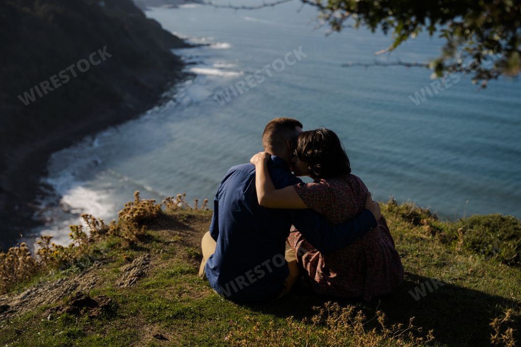 A cute young couple sitting on the grass on a cliff next to a tree