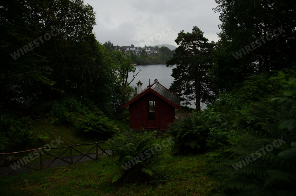 A red wooden house beside a lake on a gloomy sky background