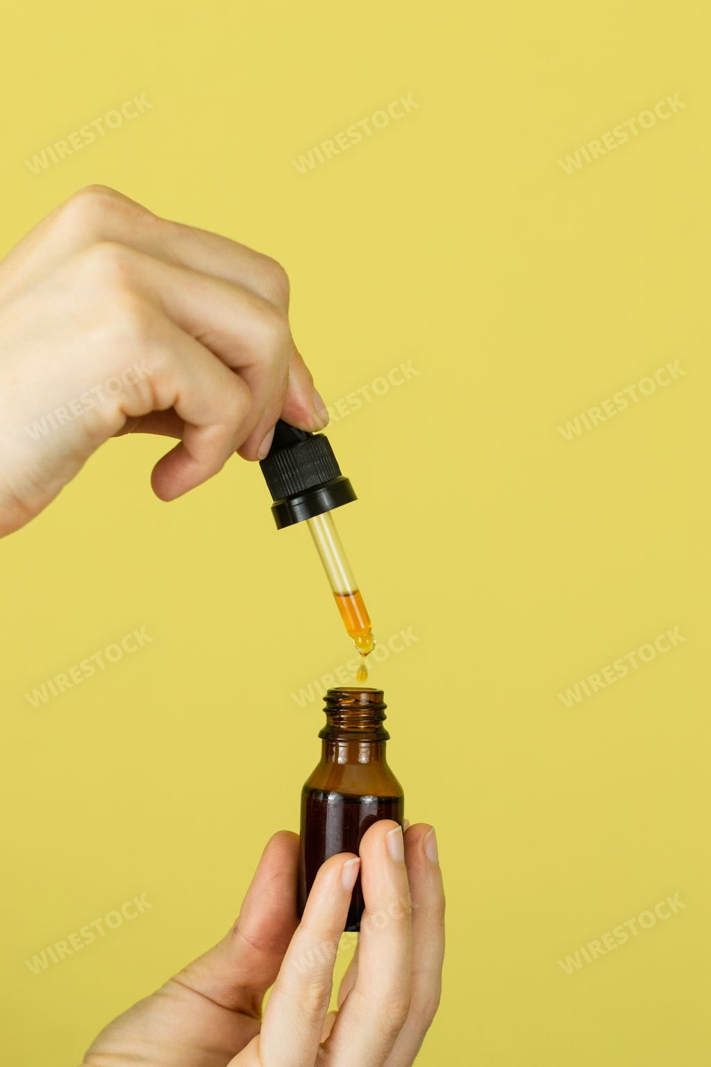 The two hands holding a dropper. A drop in the foreground falling