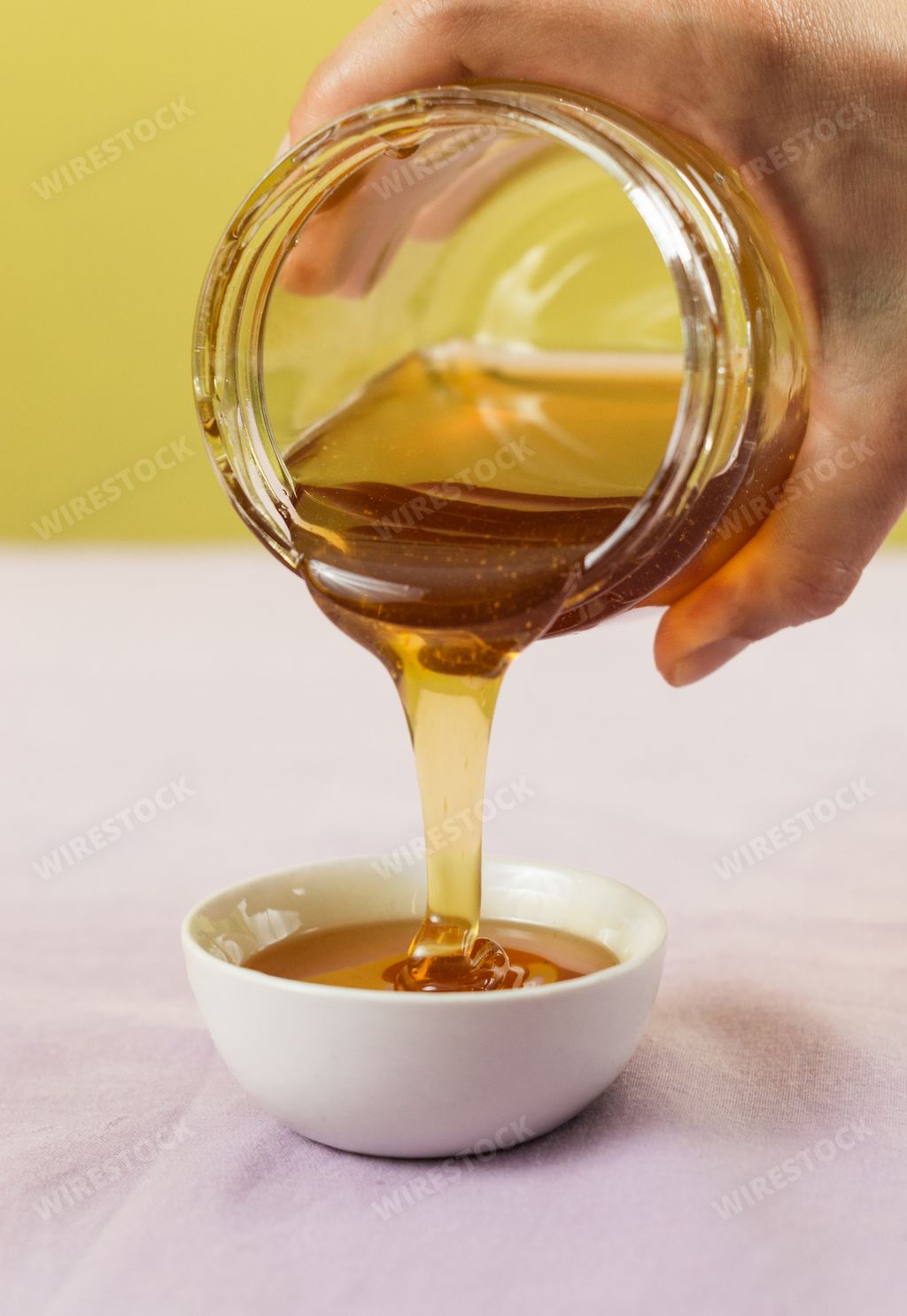 A hand pouring honey from a jar over a white bowl