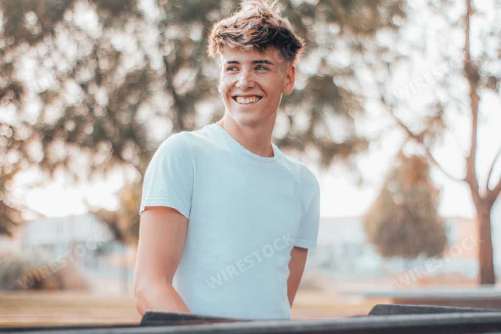 A young Spanish guy with blonde hair with a big smile in a park in daylight