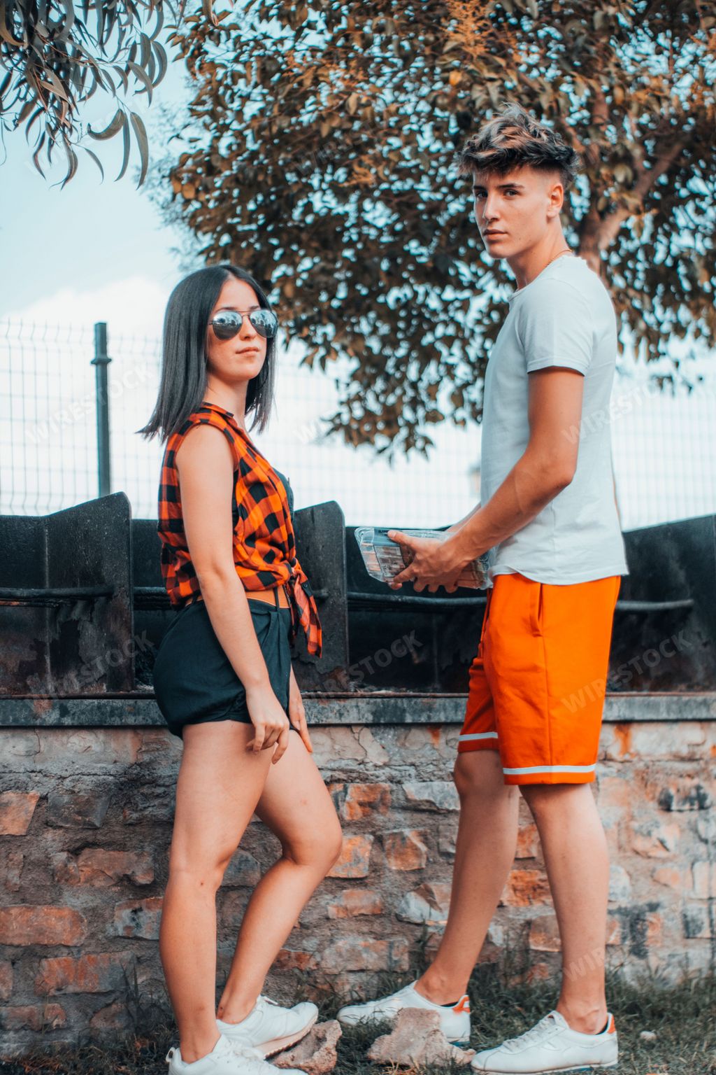 A vertical shot of two young Spanish friends spending time together while cooking in a park