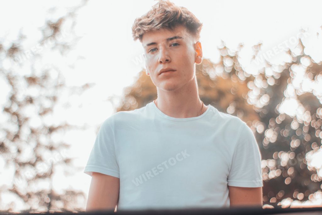 A young Spanish guy with blonde hair wearing a white shirt in a park outdoors