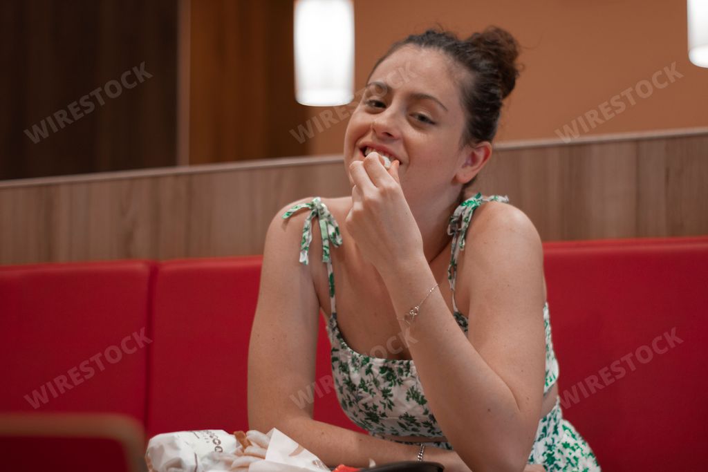 A young Caucasian brunette female smiling while sitting in the food court and eating fast food