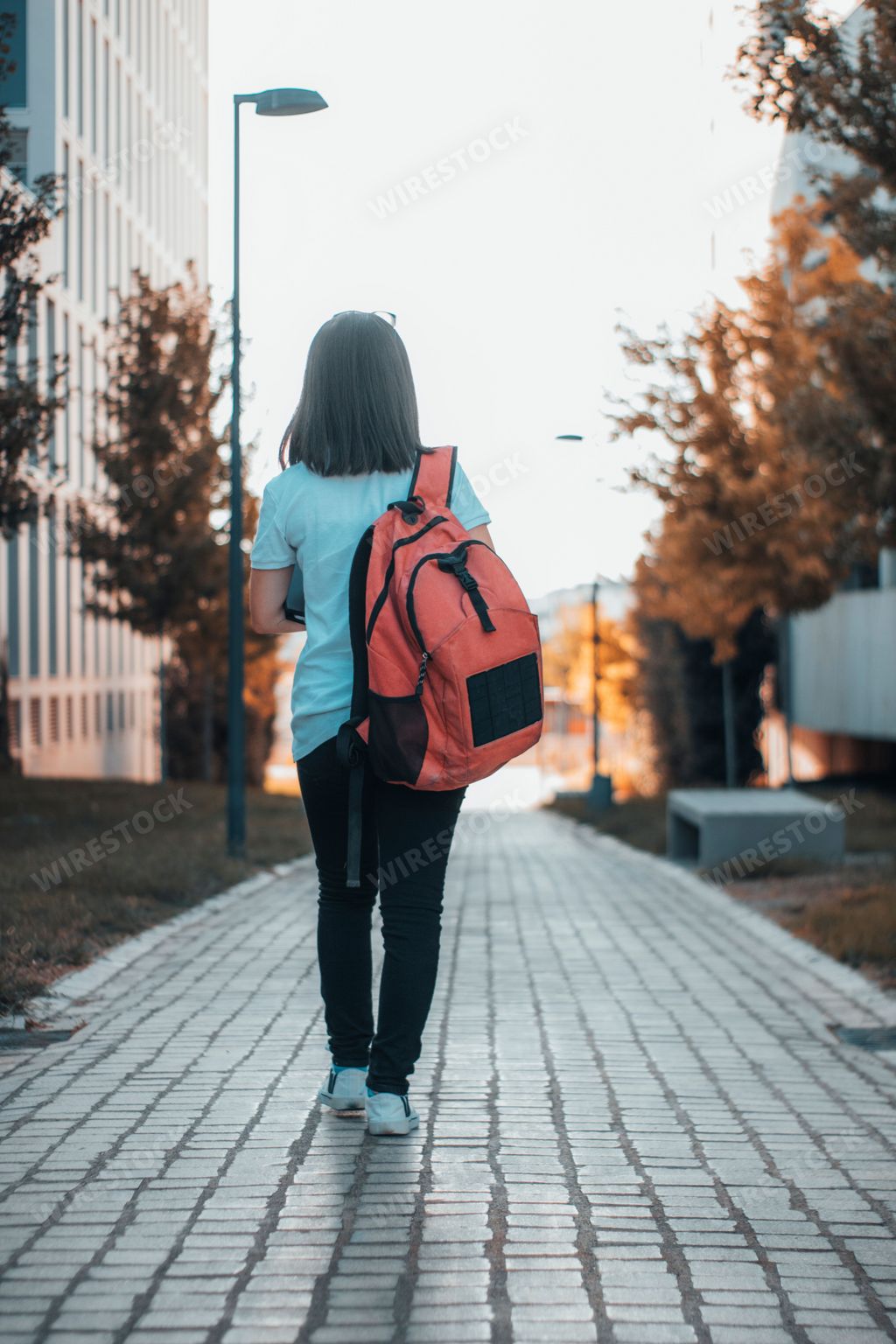 A low-angle shot of a woman with a backpack from behind walking on the pavement.