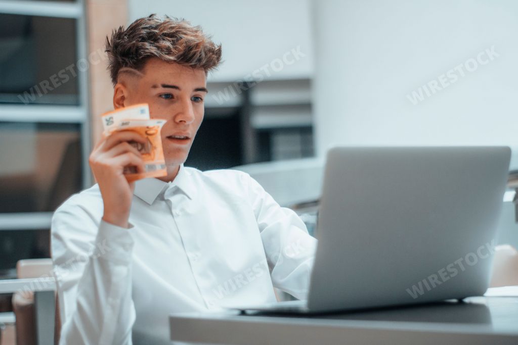 A young Spanish man holding cash Euro and working on a computer