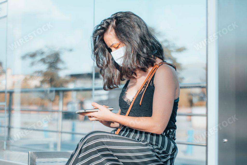Beautiful brunette woman with face mask sitting at the subway or tram stop to travel to another destination