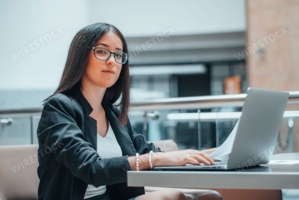 A young Spanish woman working on a laptop and looking at the camera