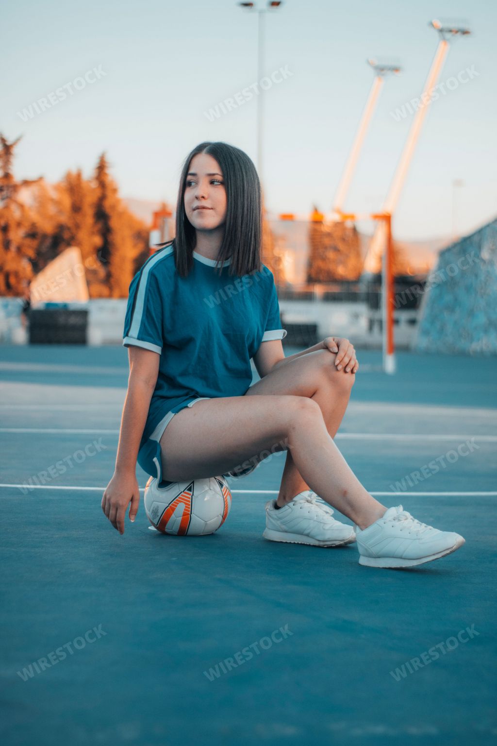 A beautiful shot of a female football player sitting on the ball on the football pitch