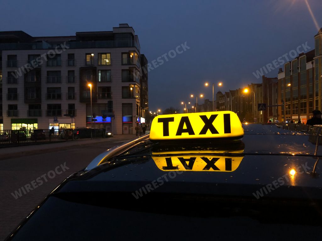 A sign of taxi on the car driving in a city at night