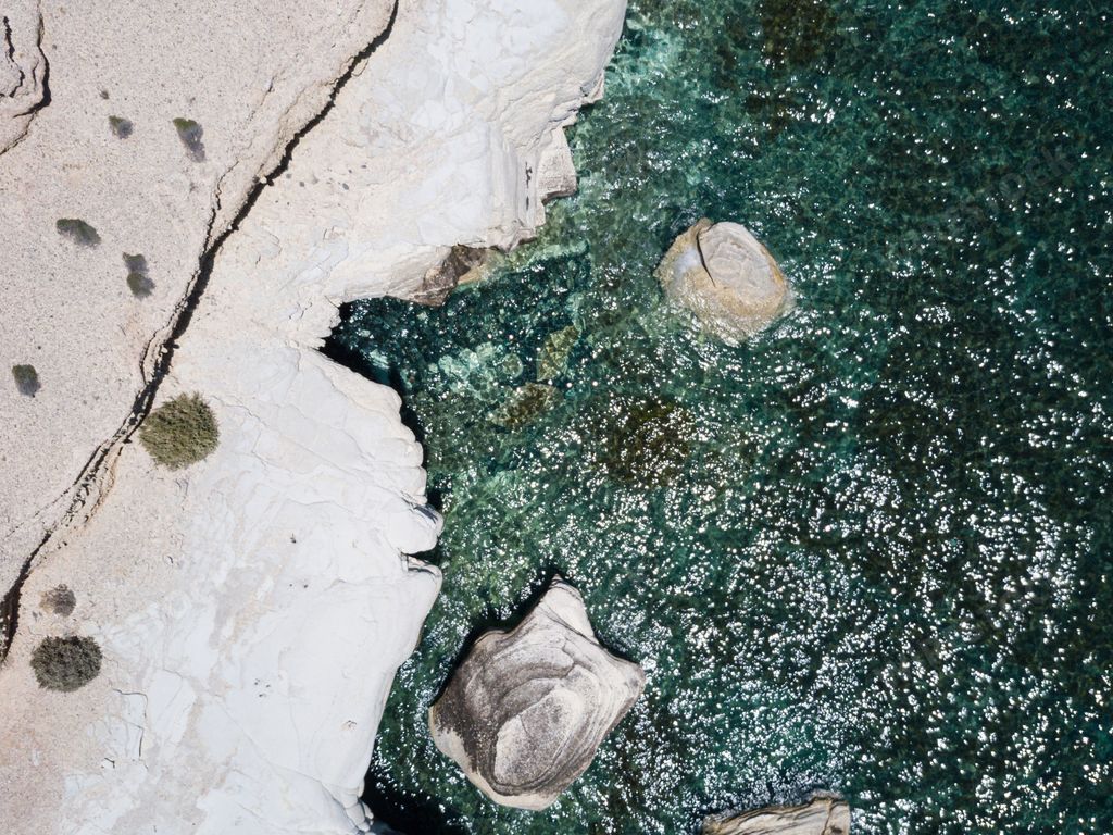An aerial overhead shot of the wavy sea with cliffs on the side