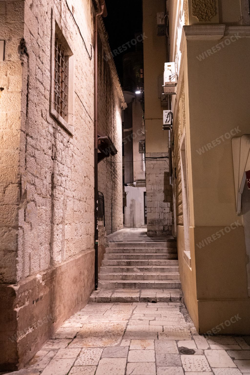 A vertical shot of stairs in an alleyway between old buildings at night