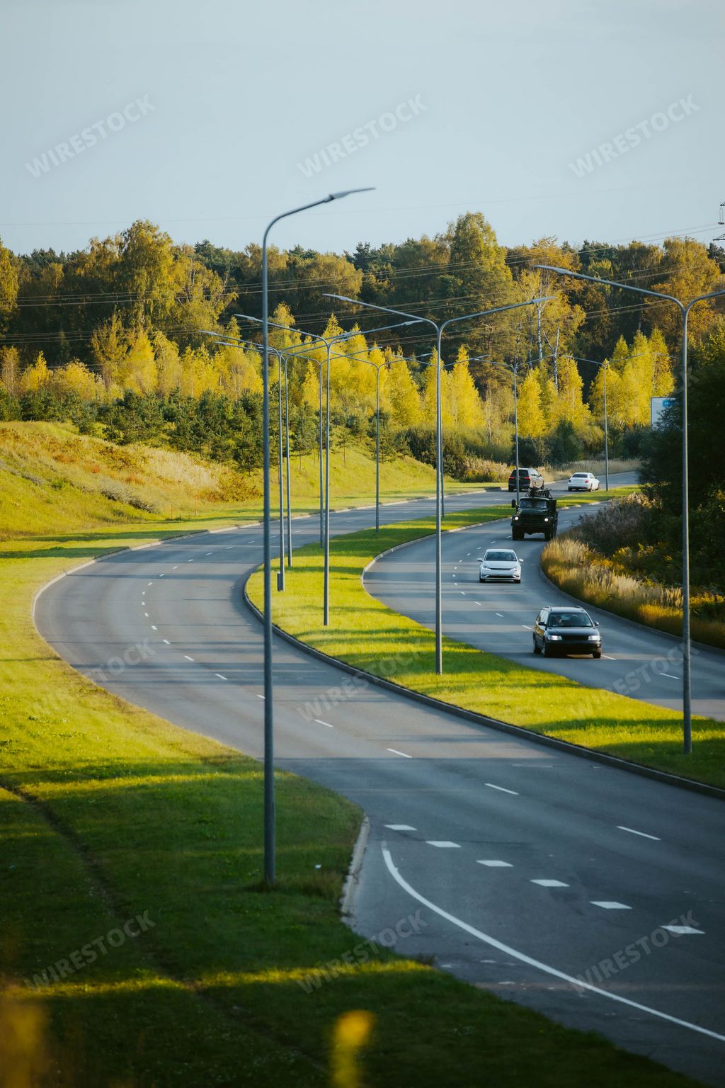 A vertical top view of cars driving along a highway road in the evening time under a sunny blue sky