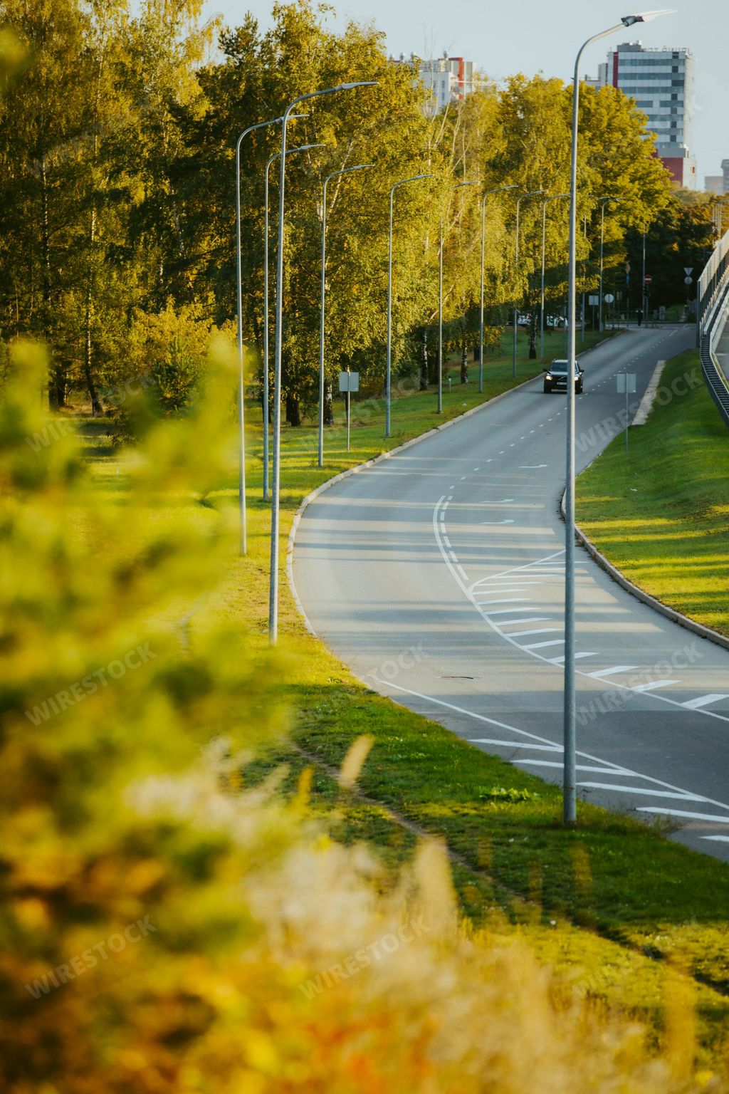 A vertical top view of a car driving along a highway road in the evening time under a sunny blue sky