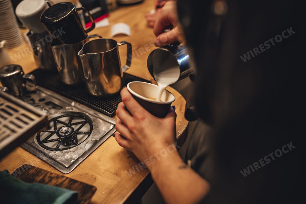 A female barista pouring milk to make a cup of cappuccino coffee in a coffee shop