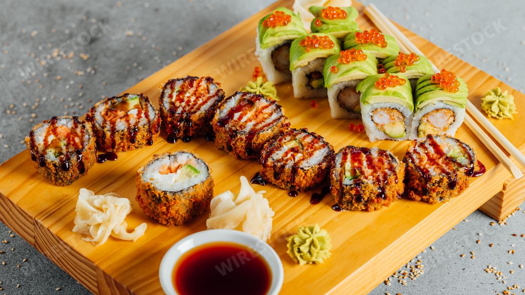 A close-up image of freshly-made sushi rolls on a wood cutting board, served with a side of traditional sushi dipping sauce