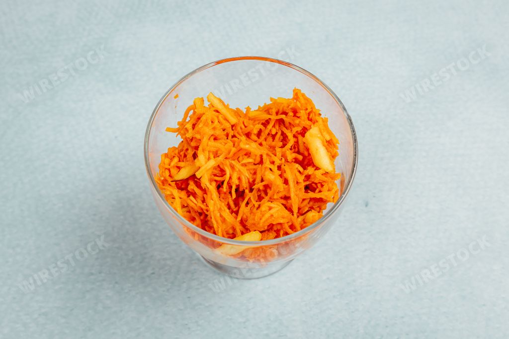 A closeup shot of grated carrot in a glass bowl on a turquoise surface
